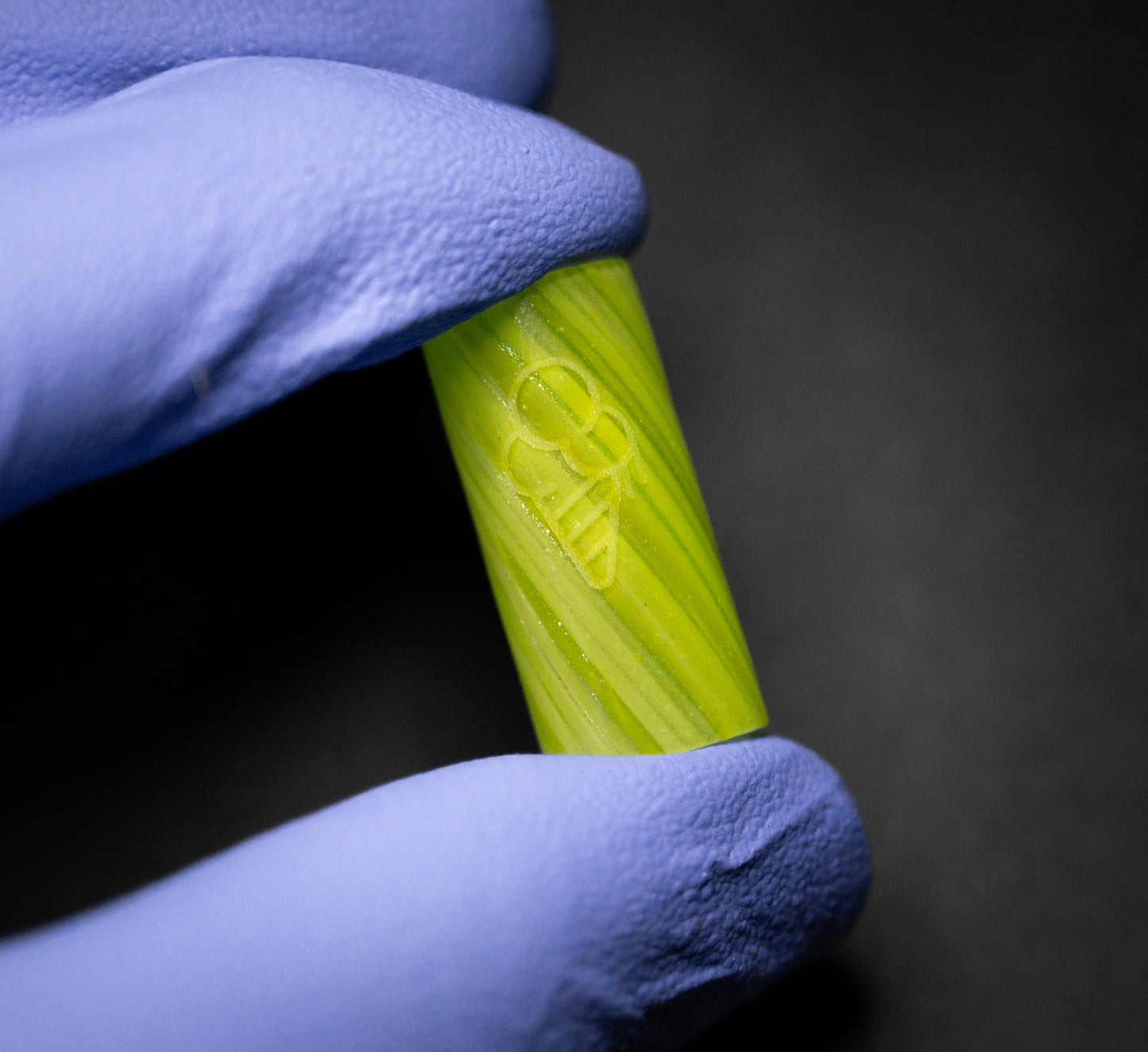 A gloved hand holds a small, cylindrical GREEN 12MM STRAIGHT piece by CONEZ with subtle markings. The dark background highlights the object.