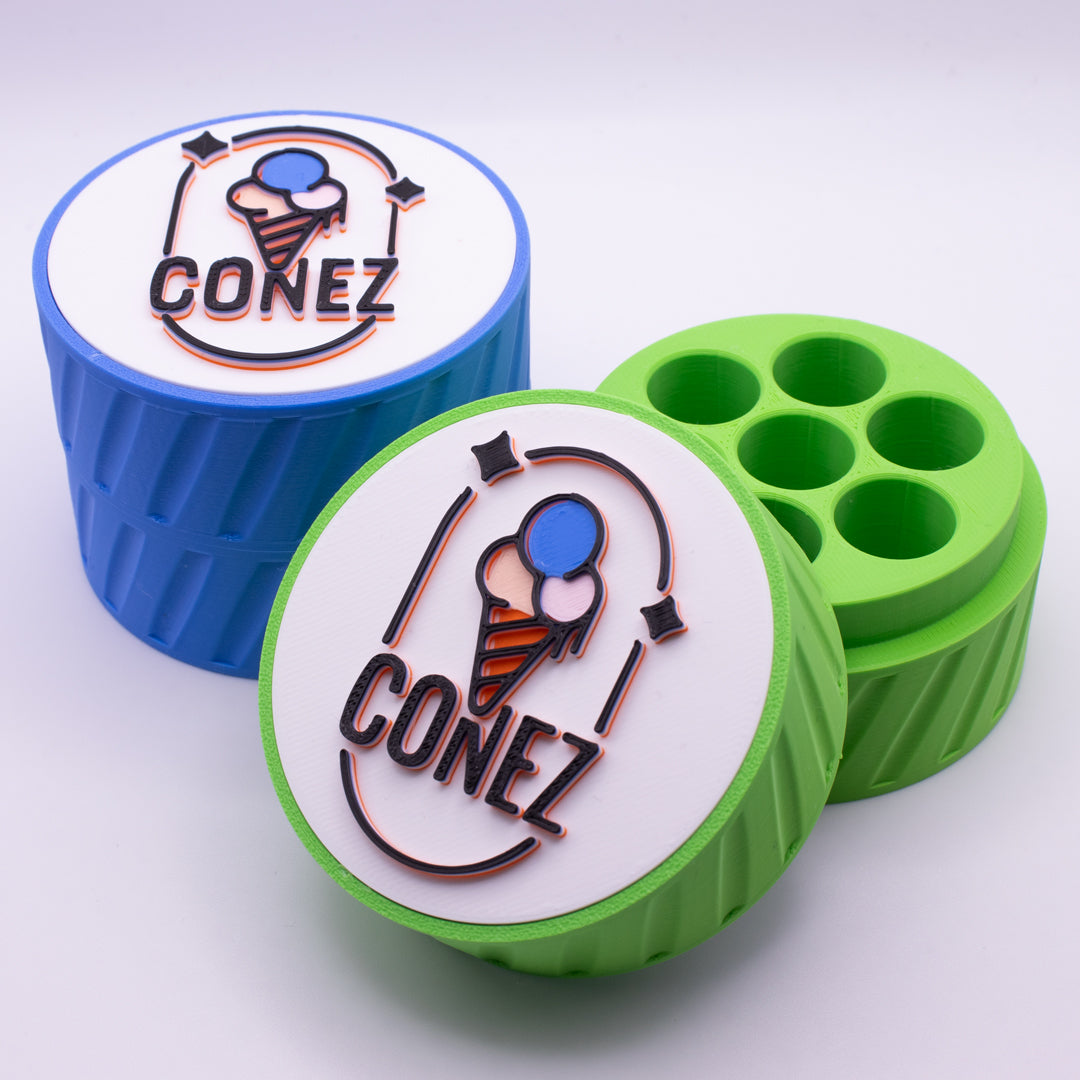Two TRAVEL CASE cylindrical containers by CONEZ, each featuring a logo with an ice cream cone. One is blue, the other green, both with lids off showing six circular compartments inside. The lids display the same logo design.