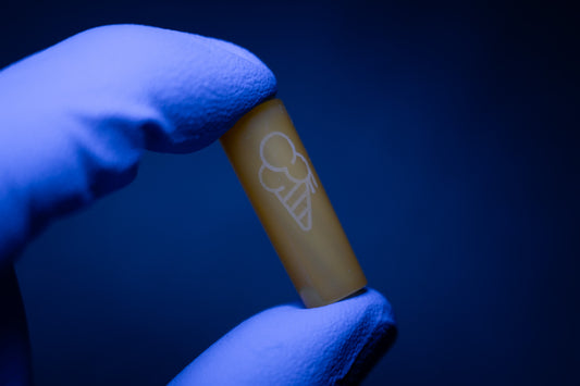 A gloved hand holds a YELLOW CONEZ capsule by CONEZ with an engraved ice cream cone symbol against a dark blue background.