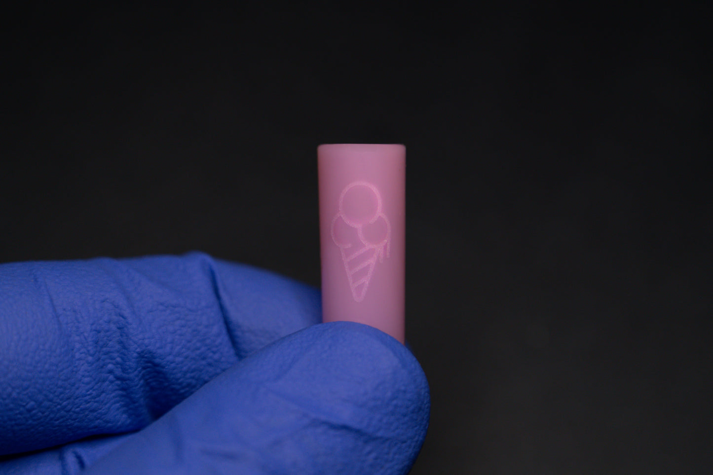 A person wearing a blue glove holds a small pink tube labeled PINK CONEZ by CONEZ, featuring an etched ice cream cone design, set against a dark background.