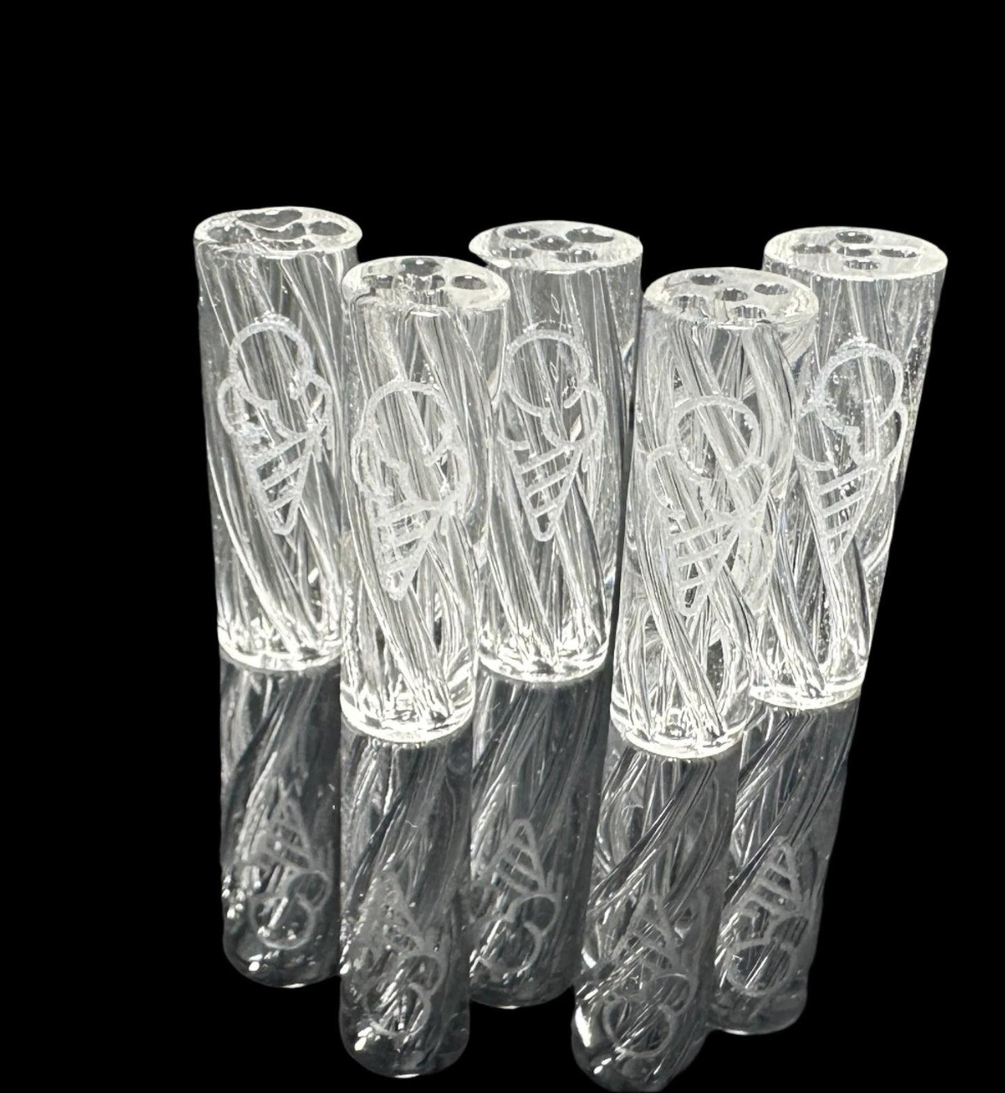 Six intricately designed, transparent objects from the CLEAR CONEZ 3 PACK by CONEZ are crafted from durable borosilicate glass. These cylindrical items feature a swirling pattern and reflect light beautifully against a glossy black surface.